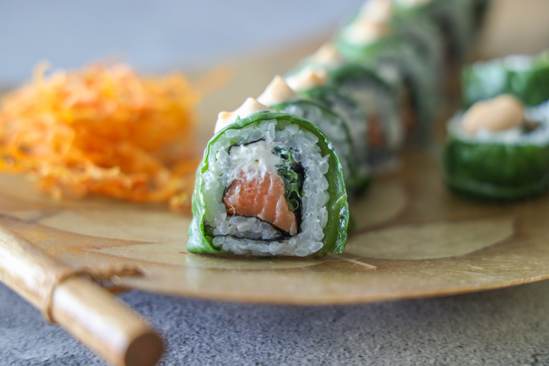 Rollos de sushi envueltos en hoja verde con salmón sobre bandeja de bambú