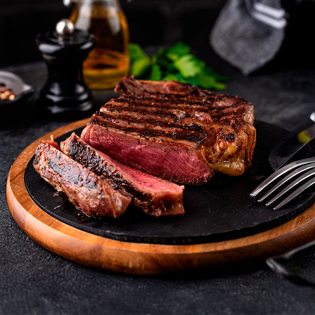 Steak a la parrilla con marcas de grill, cortado en tajadas sobre tabla de madera