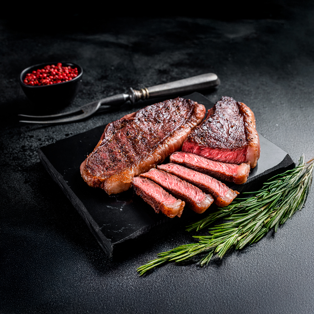 Steak a la parrilla cortado en tajadas, rosado por dentro, con romero y pimienta rosa sobre una tabla negra