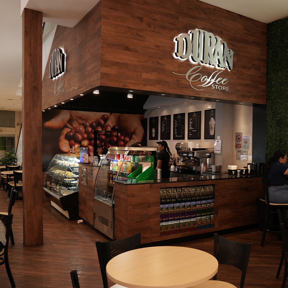 Interior de un Durán Coffee Store con barra de madera, vitrina de pastelería y mesas