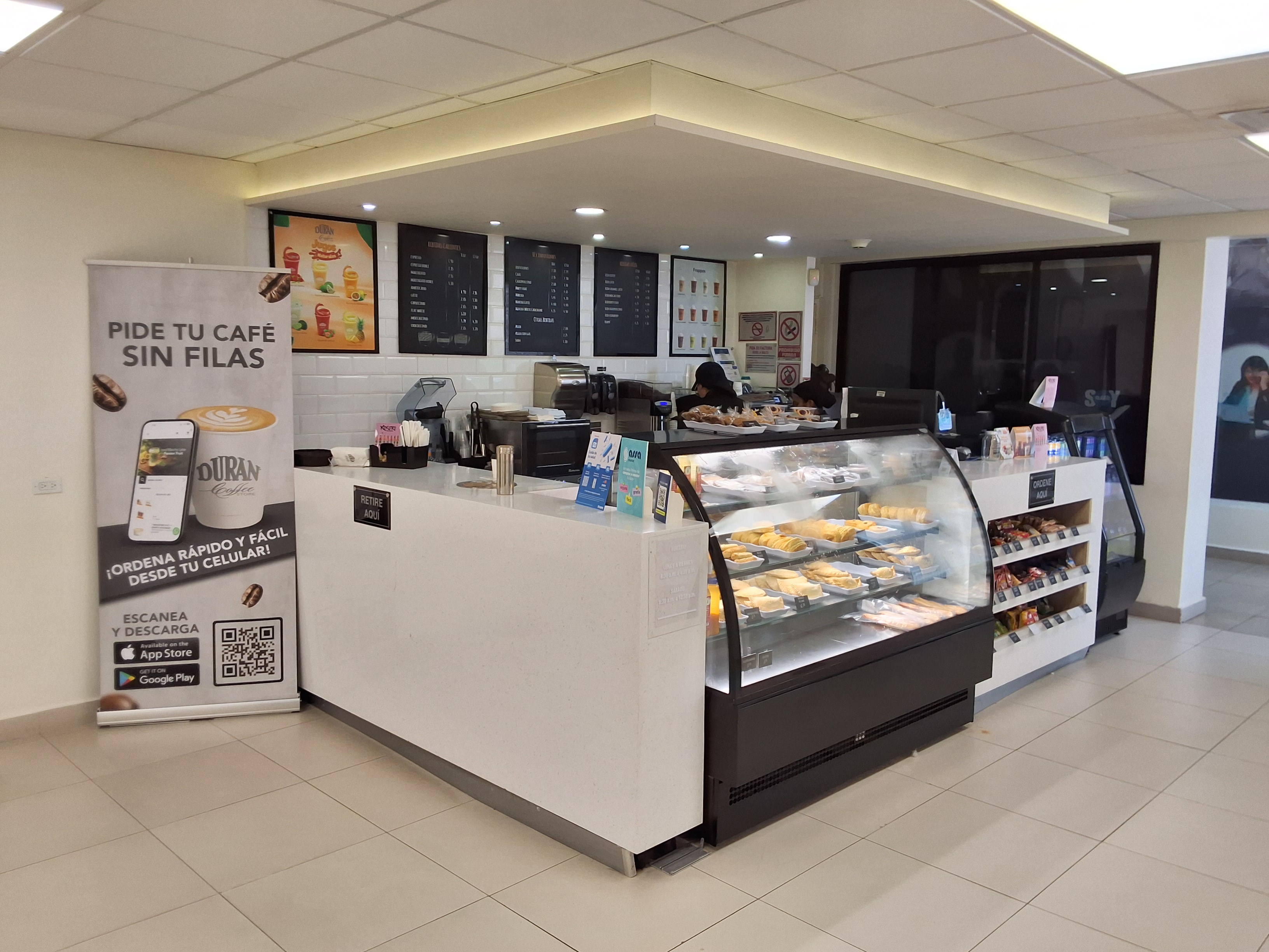 Mostrador de un Durán Coffee Store con vitrina de pastelería y banner para pedir sin filas