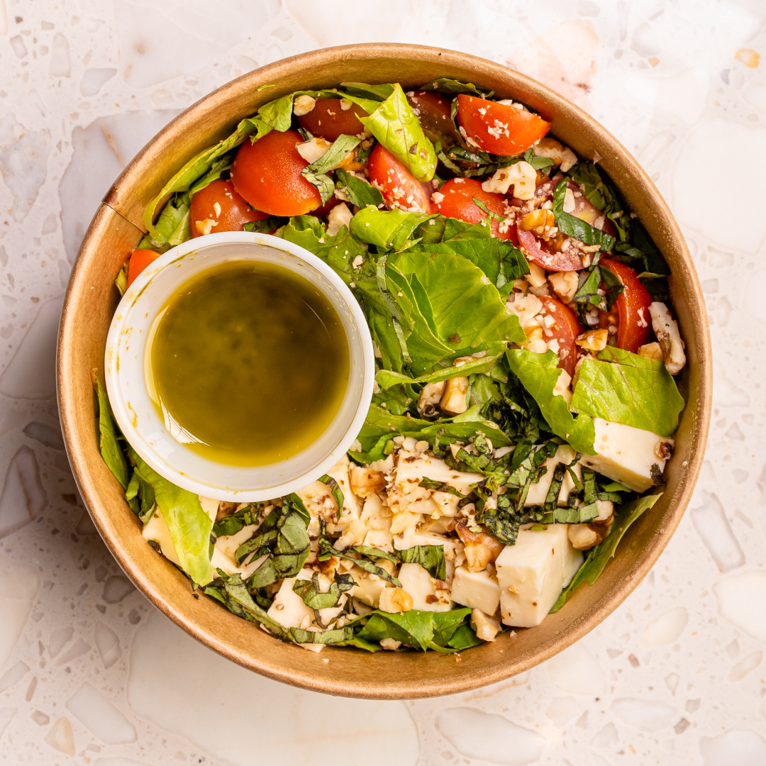Ensalada verde con queso, tomate y vinagreta en bowl para llevar