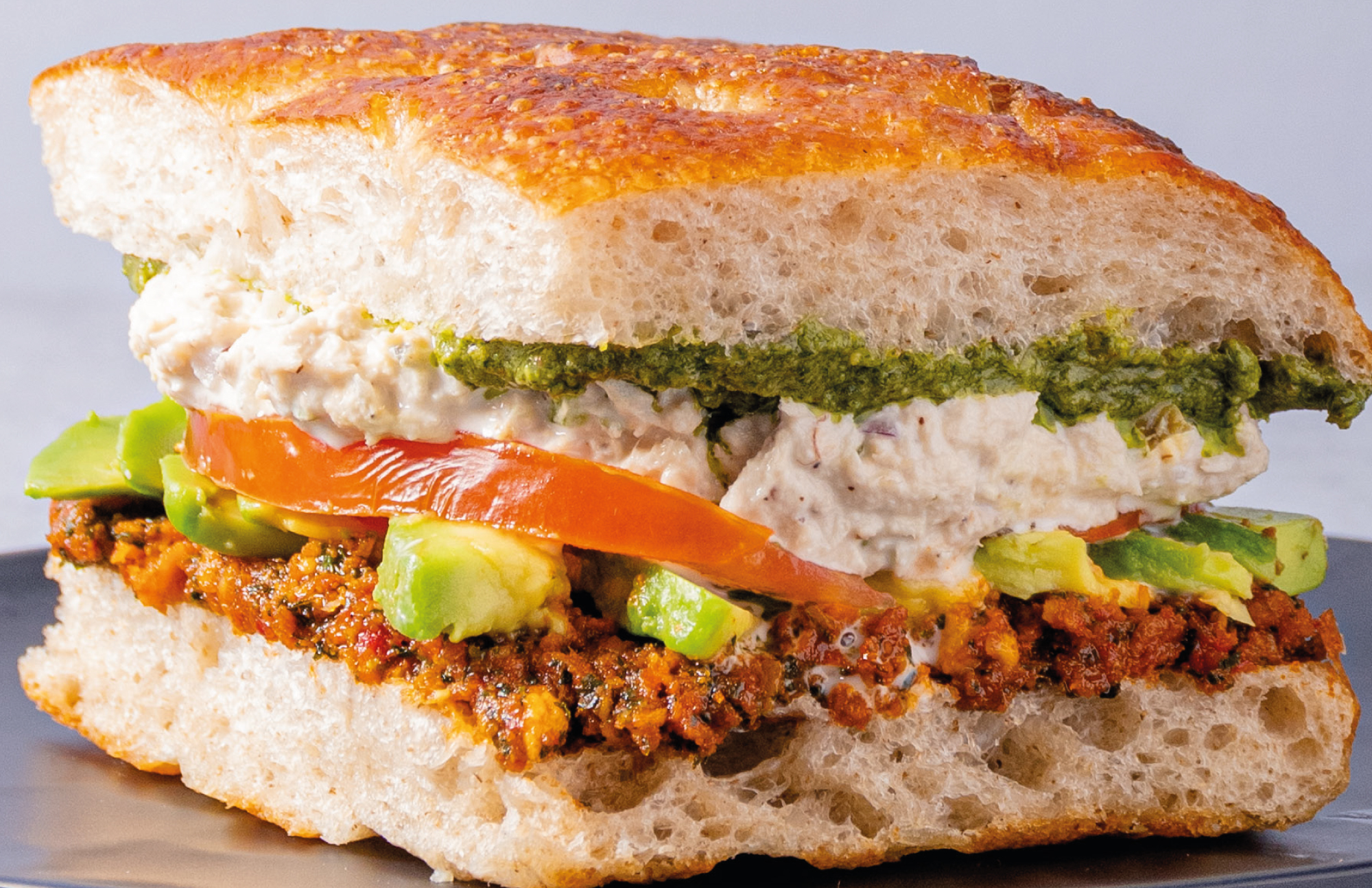 Sándwich en pan focaccia con aguacate, pesto y queso crema