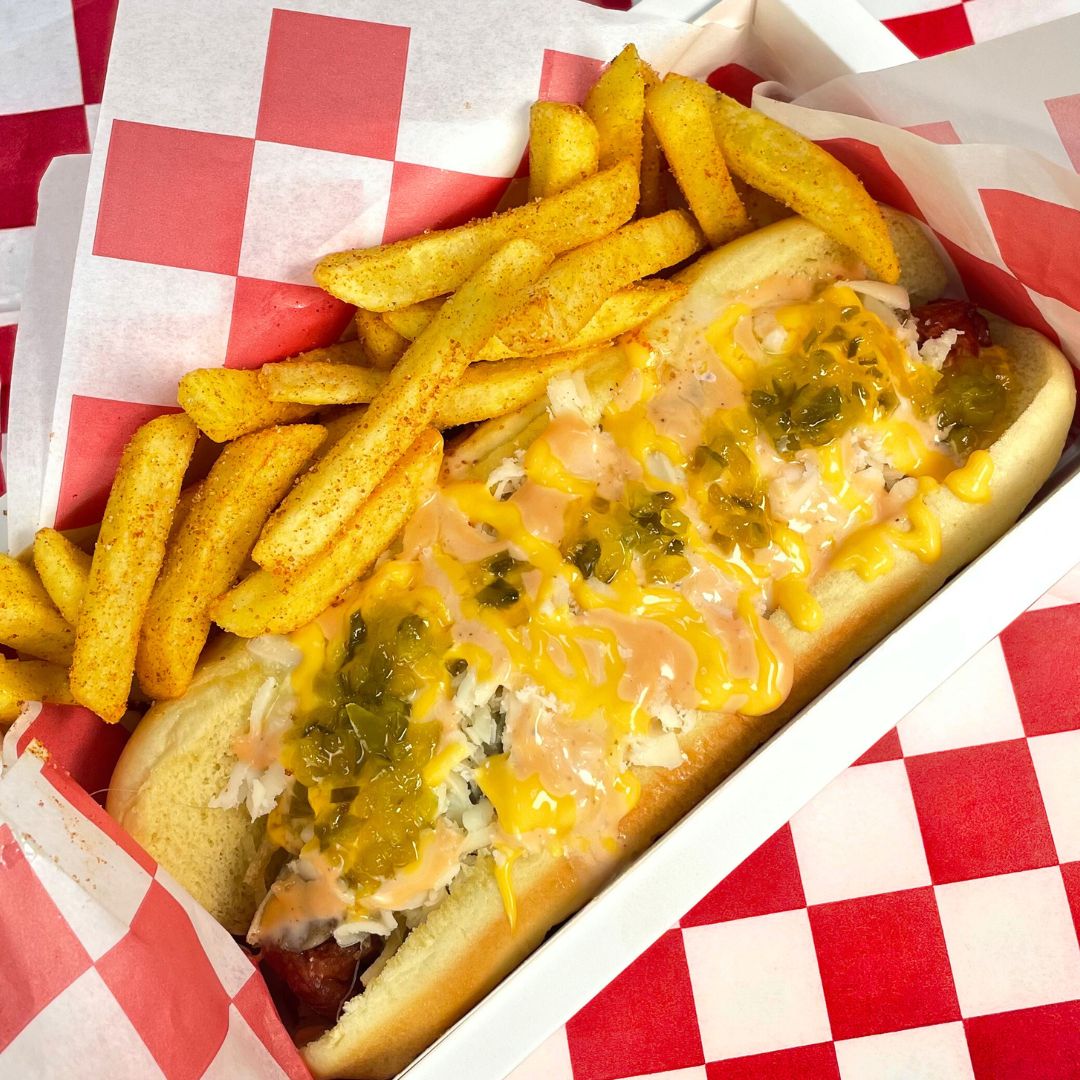 Hot dog con carne mechada y cebolla junto a papas fritas sazonadas