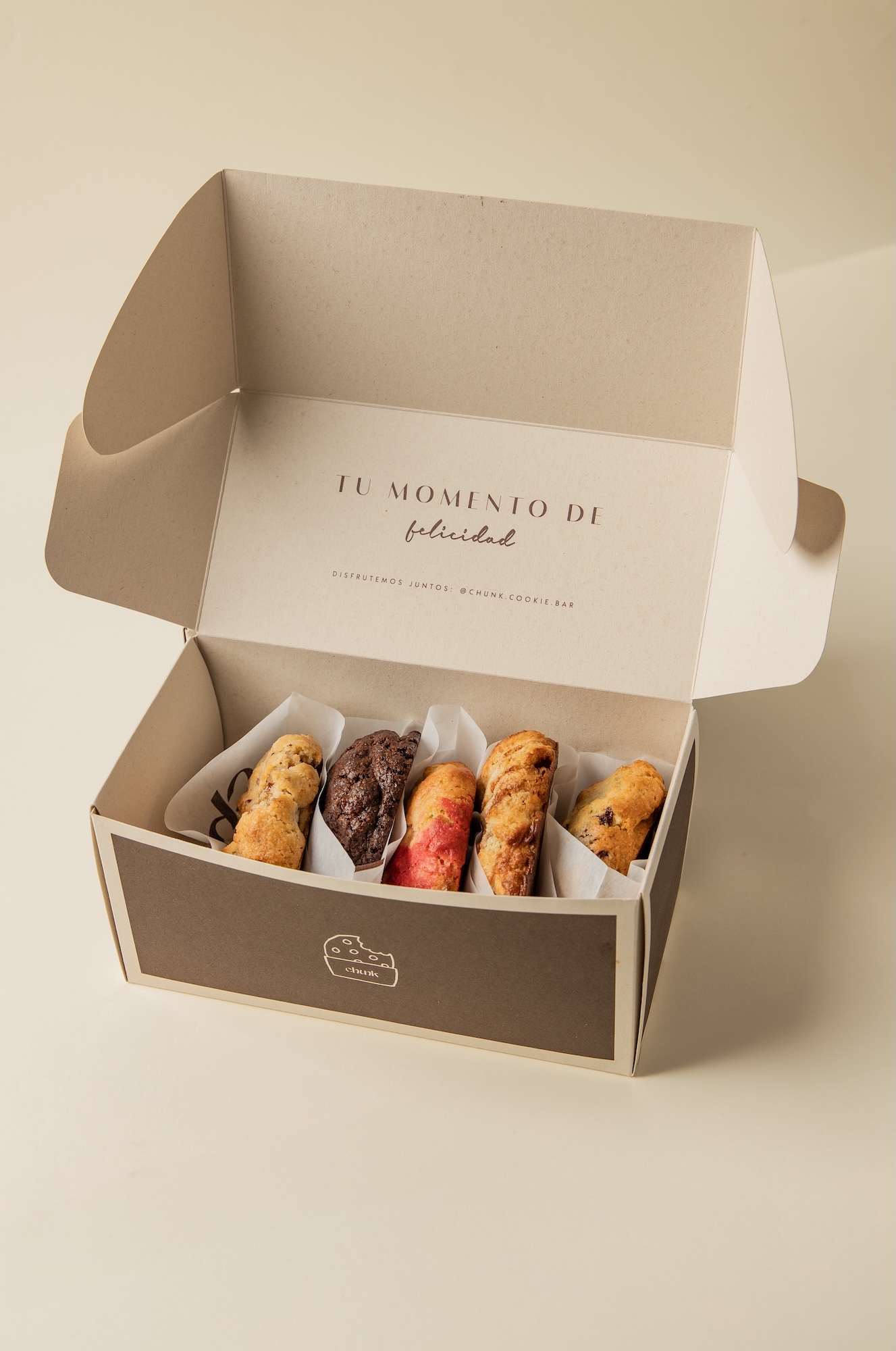Caja de Chunk cookie bar abierta con cinco cookies de distintos sabores en papel