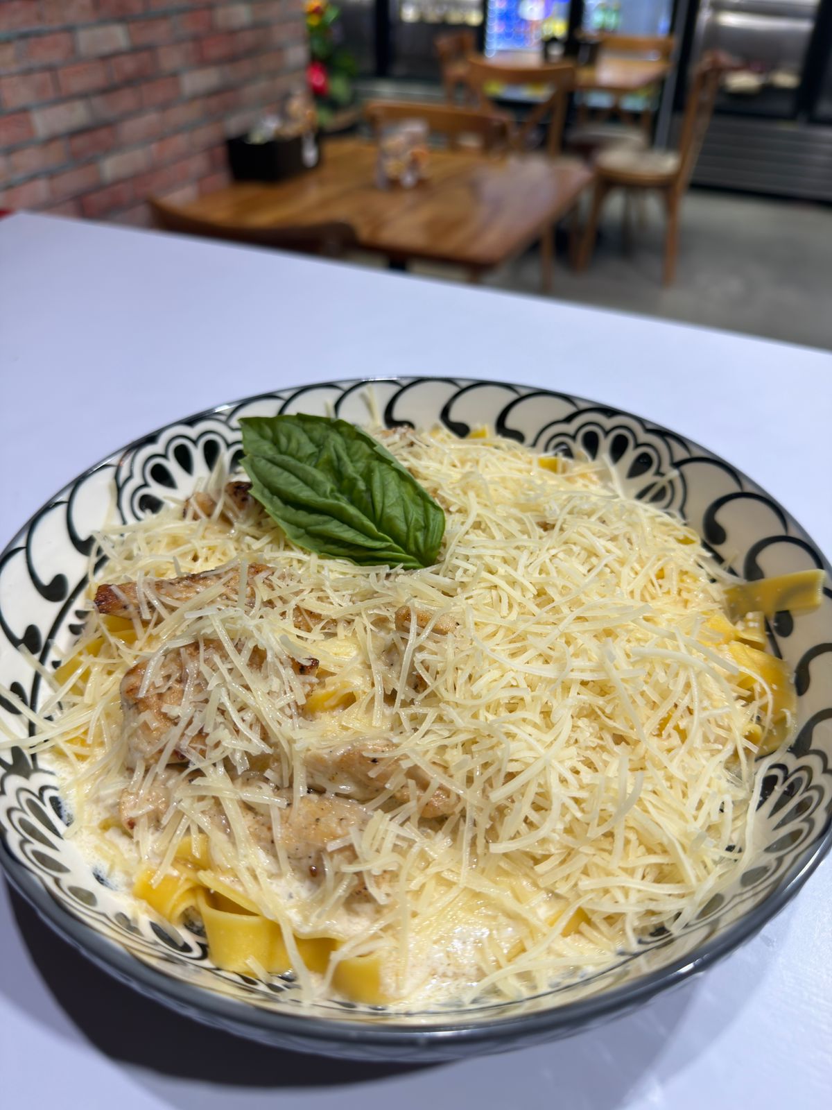 Plato de pappardelle en salsa cremosa con pollo, queso parmesano rallado y una hoja de albahaca, servido en Via Appia