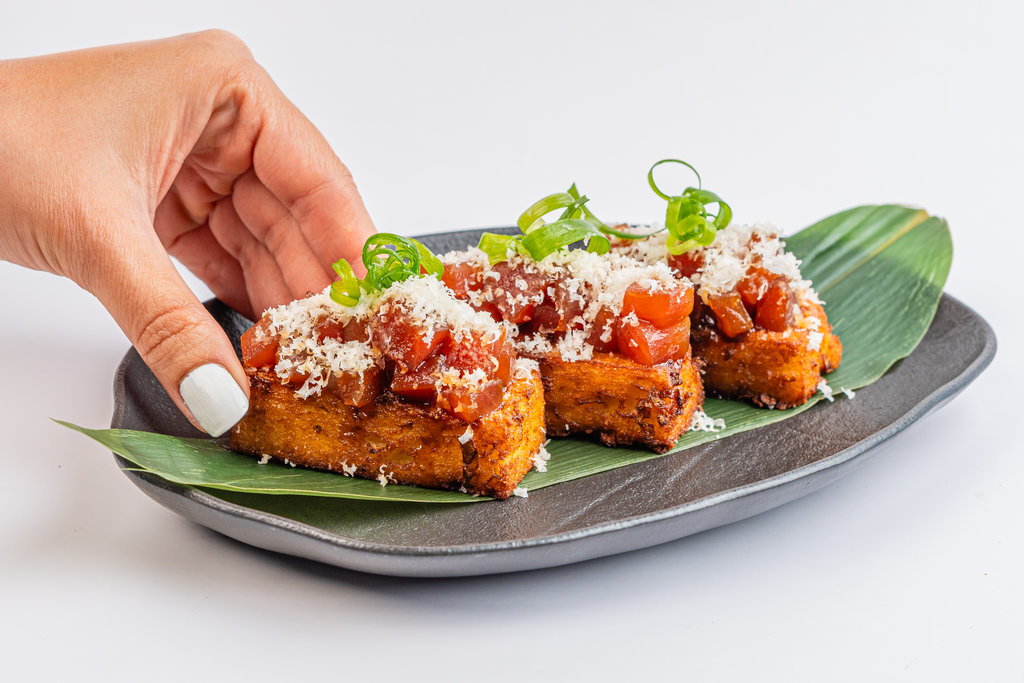 Mano tomando una tostada con tomate y queso de una bandeja para compartir