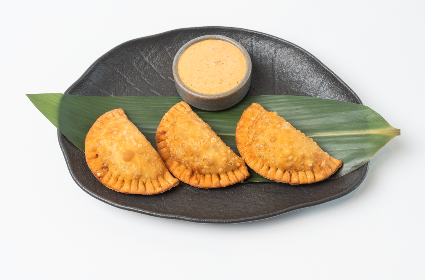 Tres empanadas doradas con salsa sobre hoja de plátano