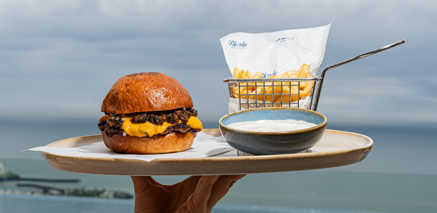 Burger con queso y papas servida en bandeja frente al mar