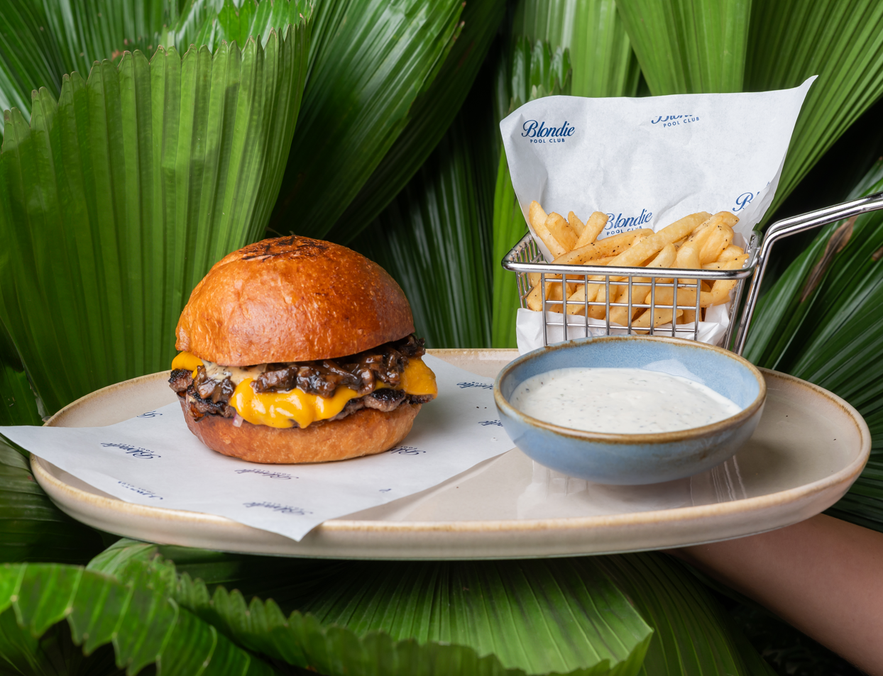 Burger con queso y papas servida en bandeja entre hojas de palma