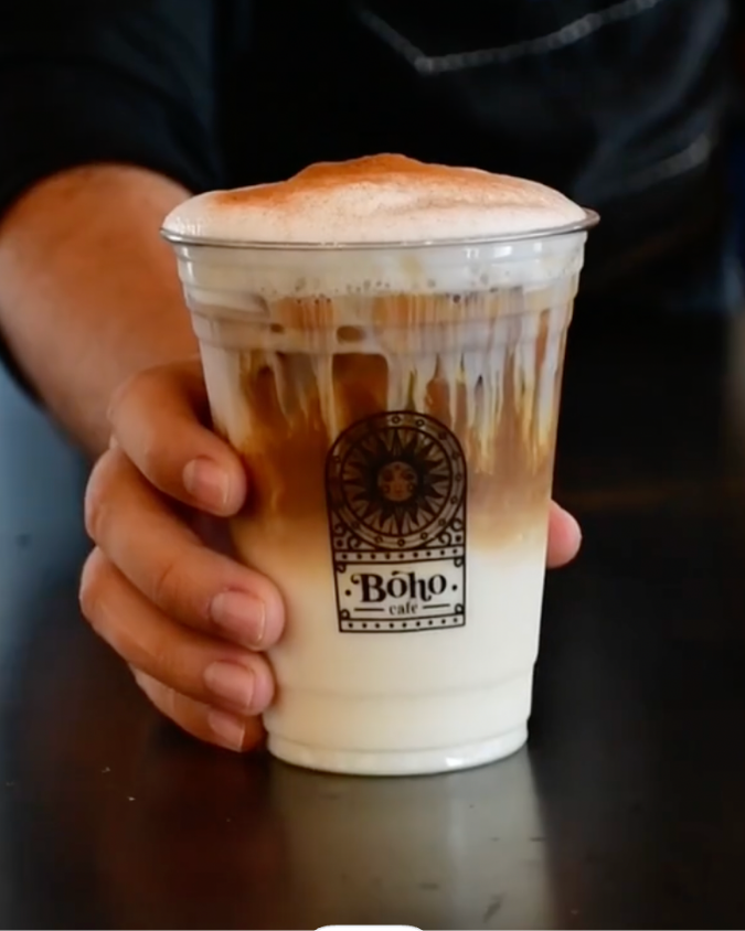 Latte frío en vaso con el logo de Boho Cafe sostenido en la mano