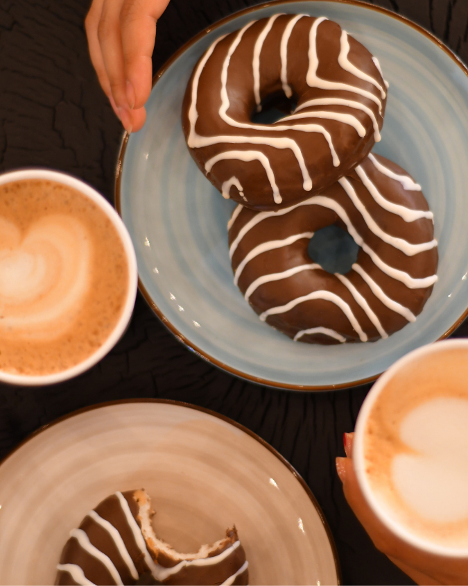 Donas de chocolate con glaseado blanco junto a dos capuchinos