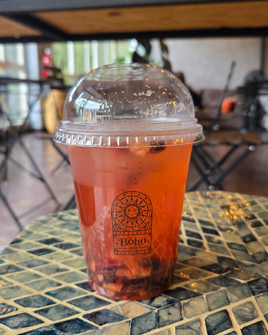 Bebida fría roja con frutos y hielo en vaso de Boho Cafe sobre mesa de mosaico