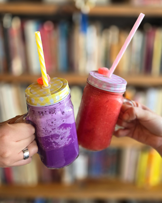 Dos bebidas frías de colores en tarros brindando frente a un librero