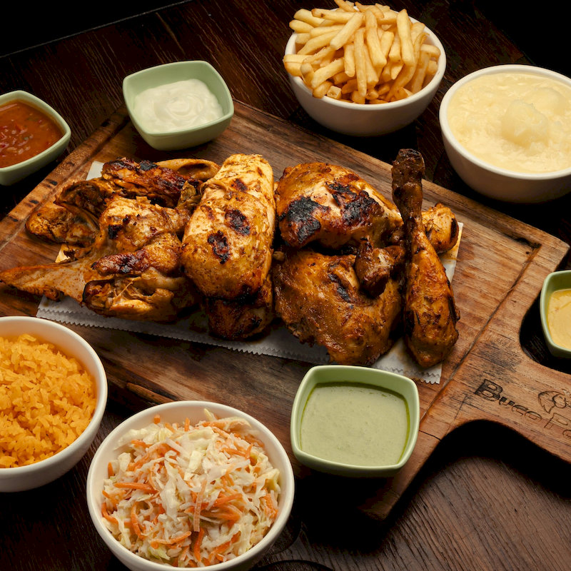 Pollo asado en tabla con papas fritas, arroz amarillo, coleslaw y salsas en bowls