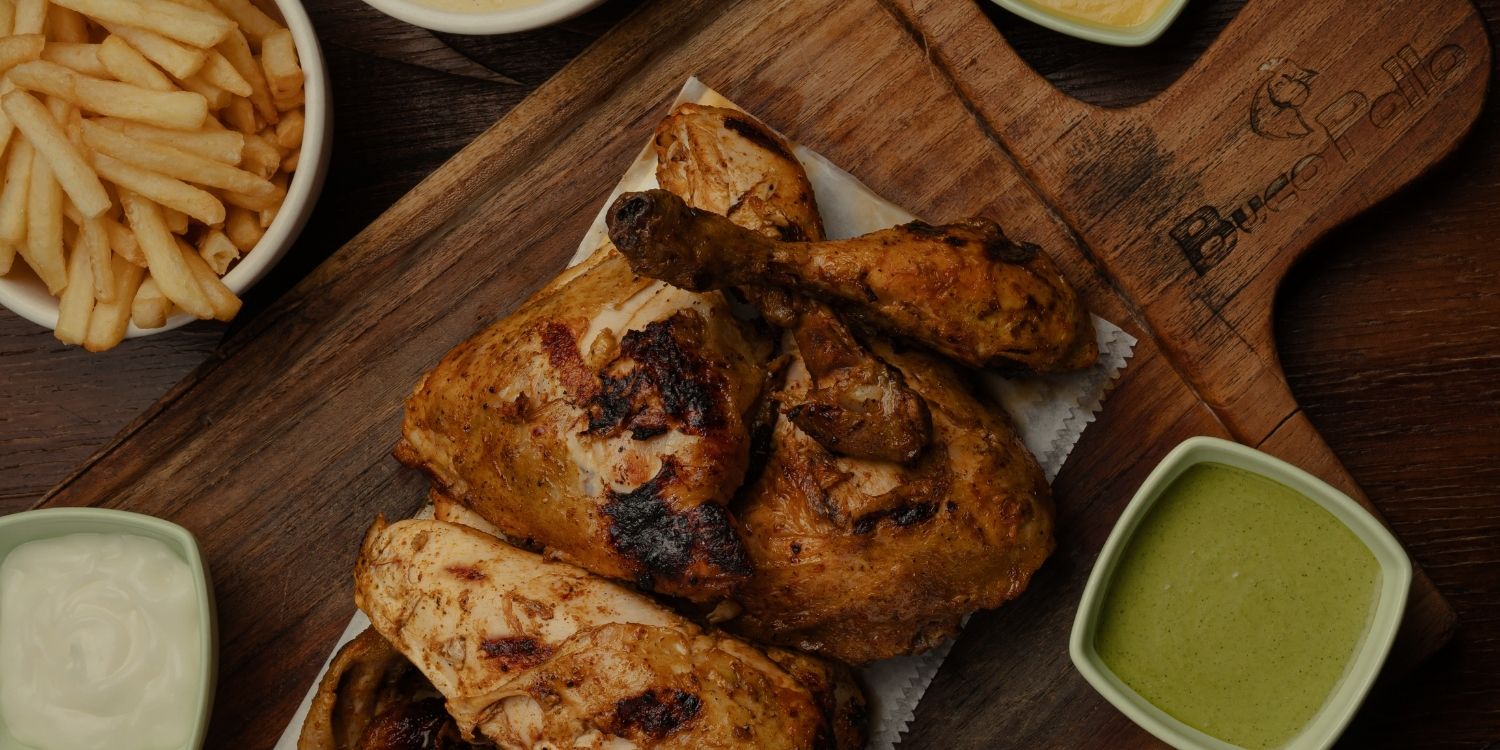 Pollo asado con papas fritas y salsas sobre tabla de madera