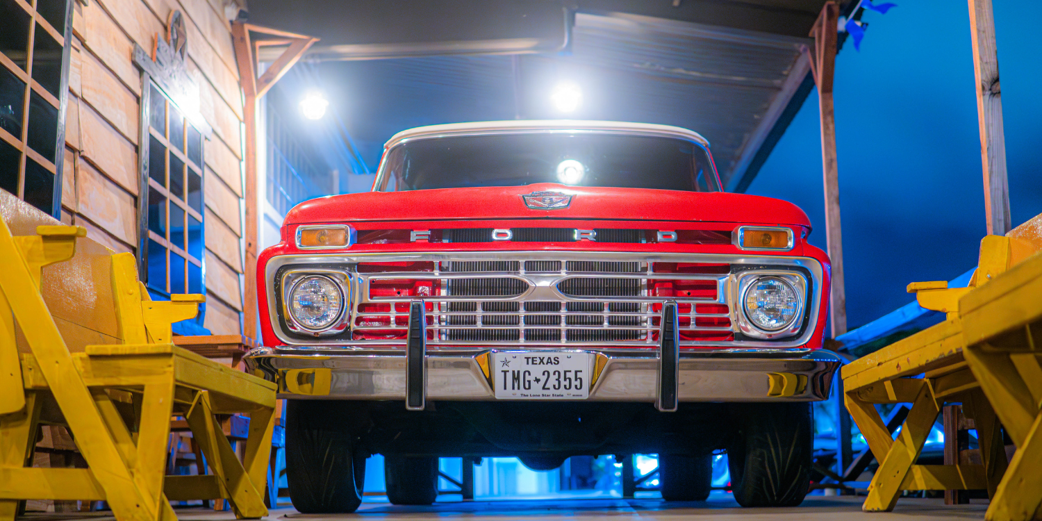 Camioneta Ford roja clásica con placa de Texas entre bancas amarillas