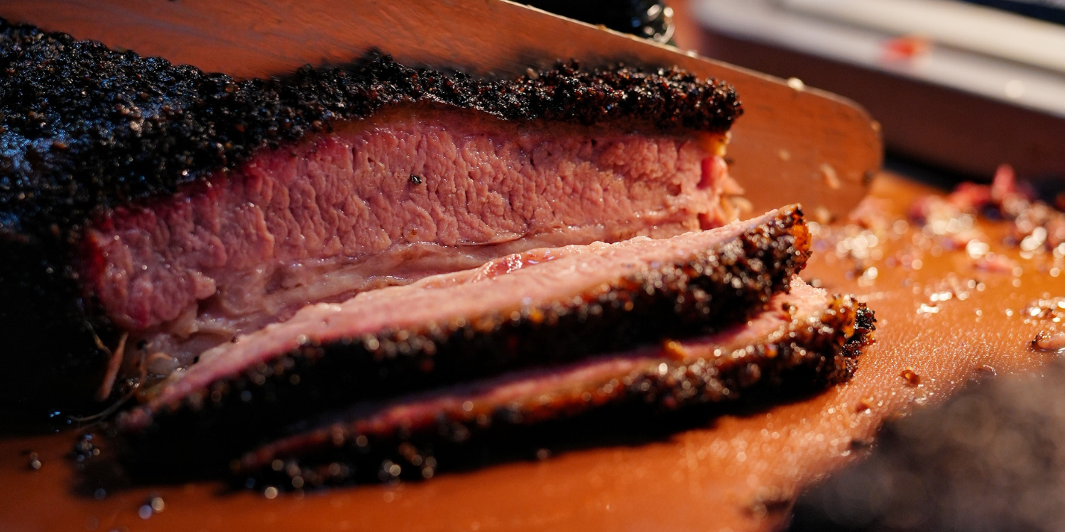 Brisket ahumado con corteza negra de pimienta recién cortado en tablas sobre la tabla de madera
