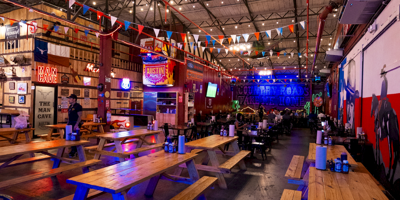 Salón de Austin Mama's con mesas largas de madera, banderines de colores y letreros de neón