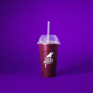 Smoothie de açaí OAKBERRY con tapa y pajilla sobre fondo morado