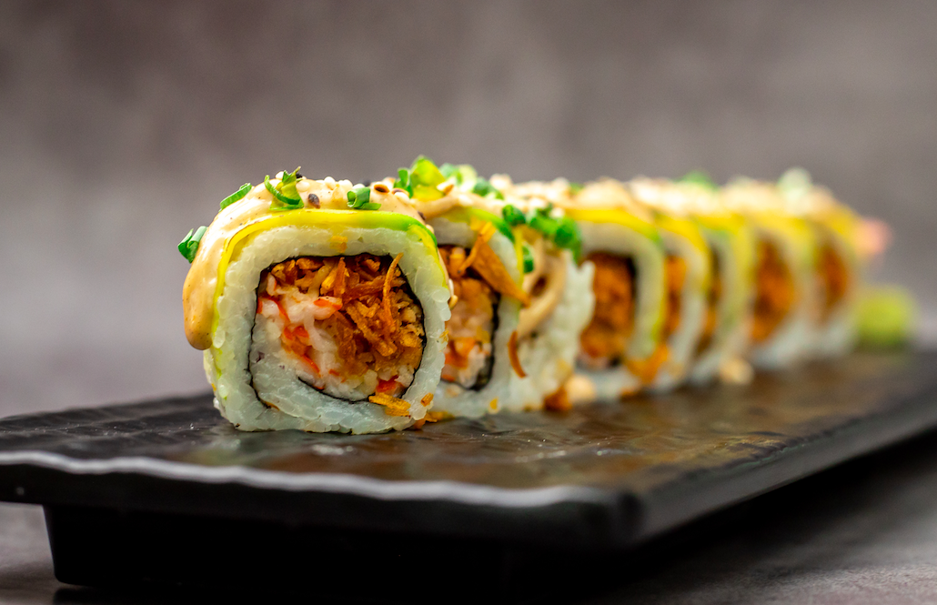 Roll de Sushi Rocket cubierto de aguacate y mango sobre pizarra negra