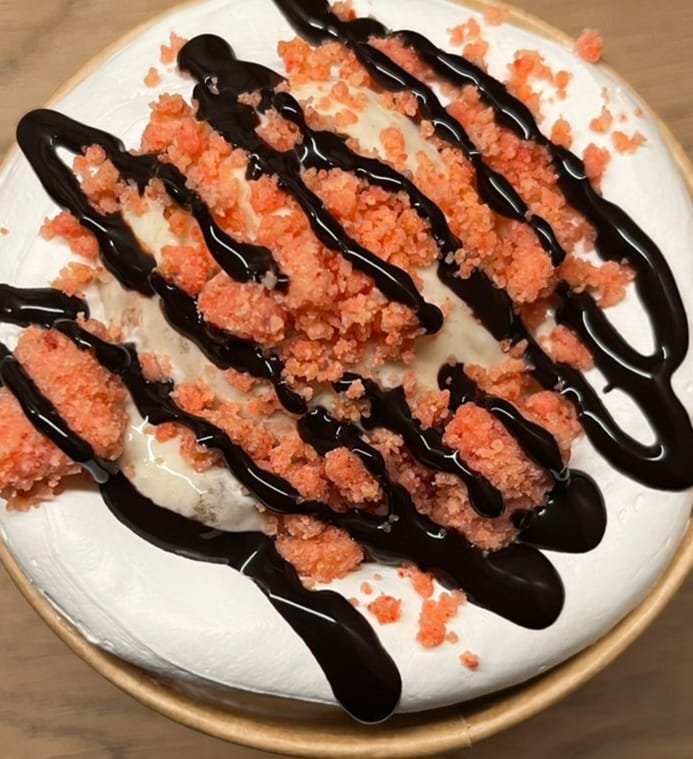 Postre cremoso con crumble rosado y hilos de chocolate