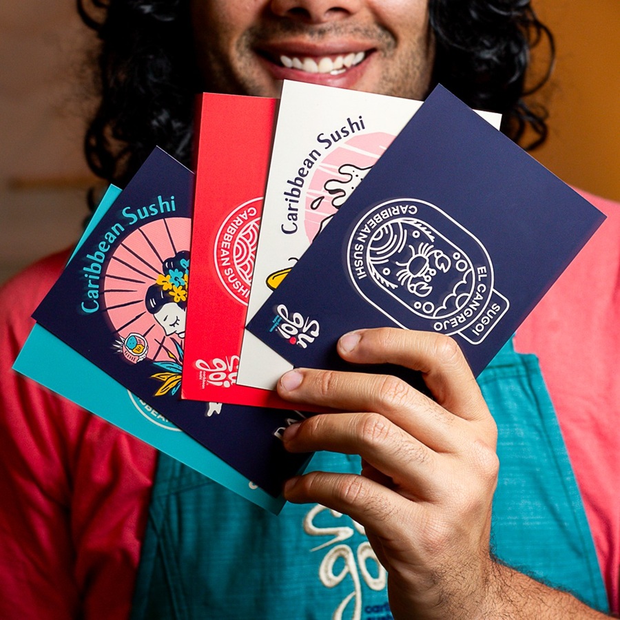Integrante de Sugoi sonriendo con las postales ilustradas de Caribbean Sushi en la mano